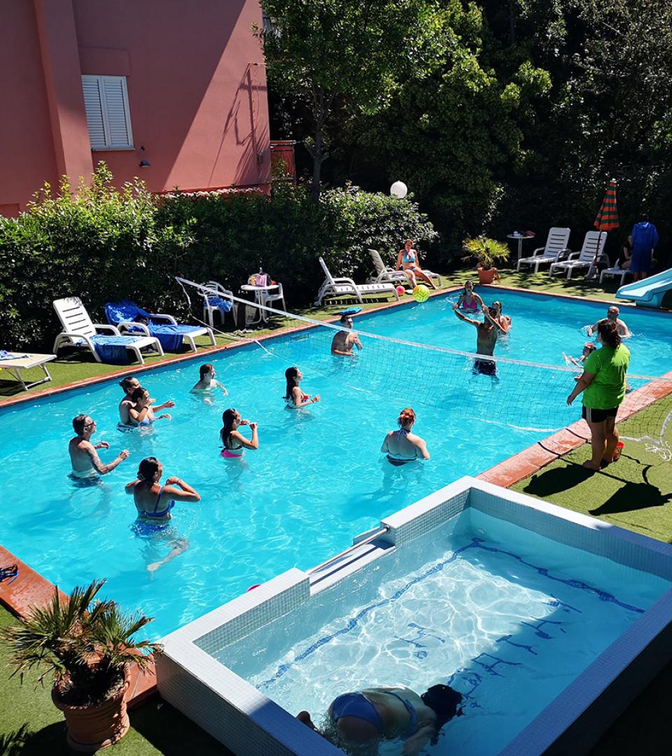 Persone giocano a pallavolo in piscina sotto il sole estivo.